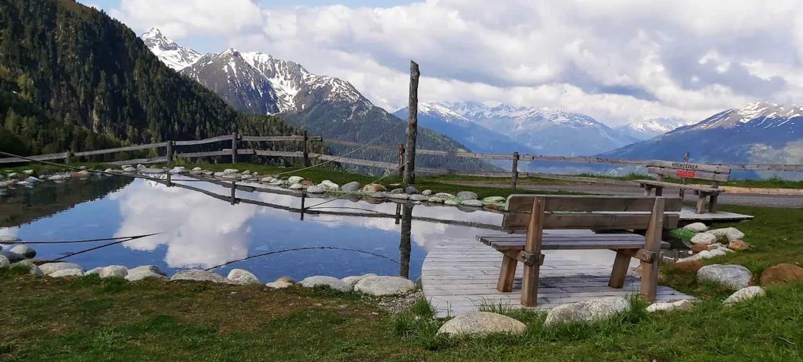 Bergsee mit Holzsteg und Bank vor Gipfelpanorama